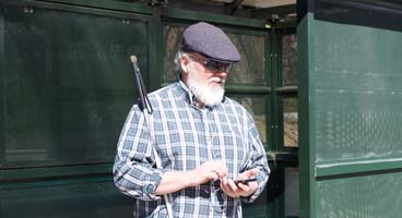 An older blind man listens to NFB-NEWSLINE on his phone while waiting at a bus stop.