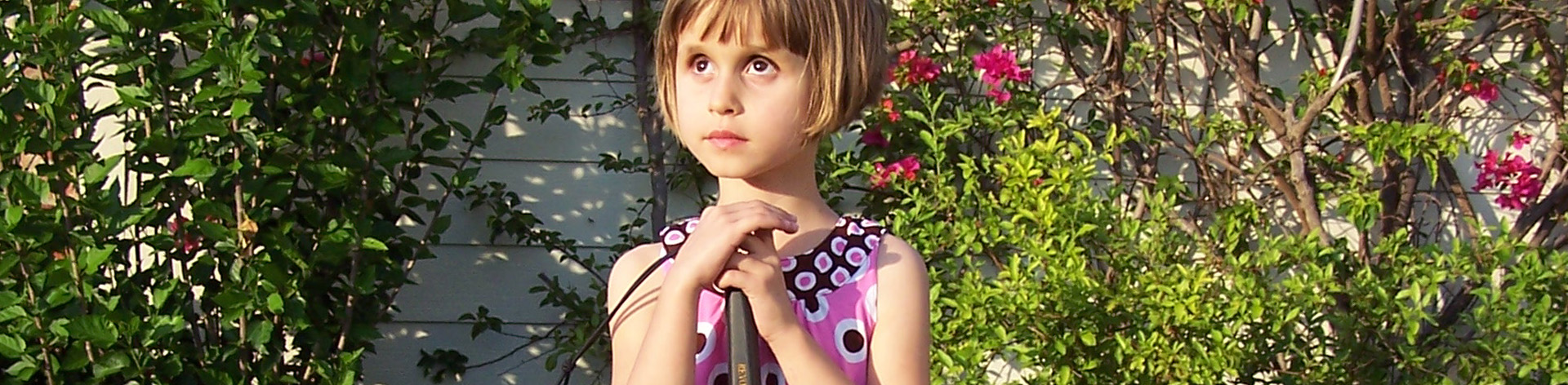 A young blind girl stands with her long white cane.