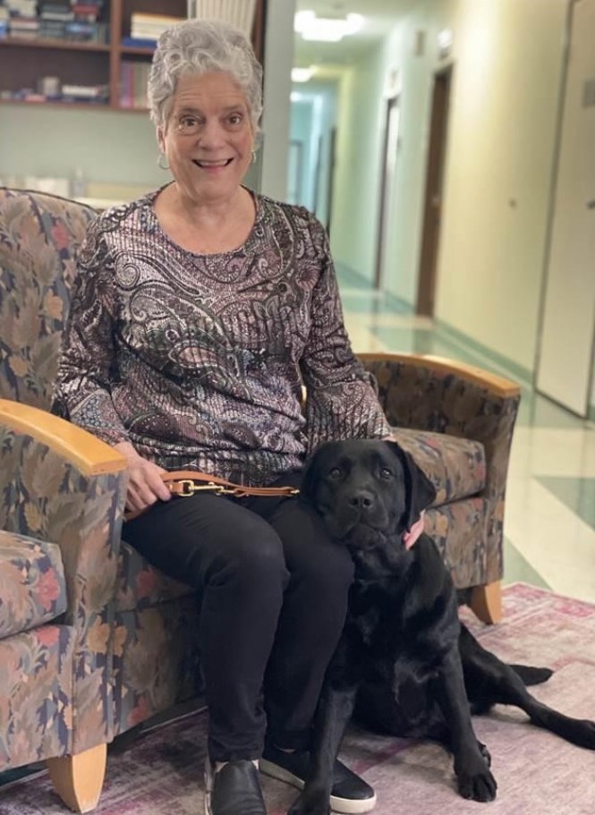 Mrs. Williams sits in a floral chair with her guide dog at her feet.